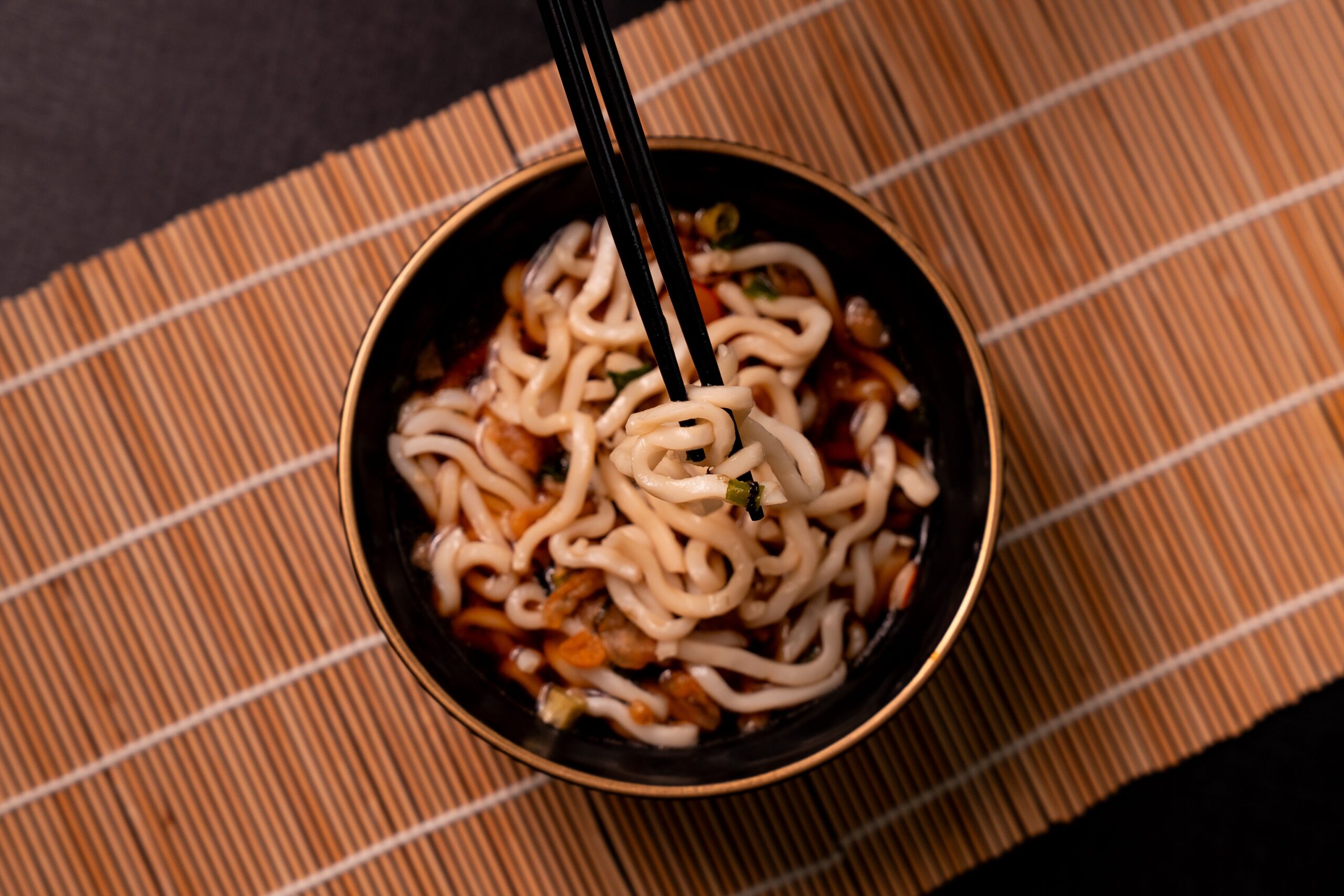 Close-up of udon noodles in a black bowl on bamboo mat, perfect for Japanese cuisine themes.