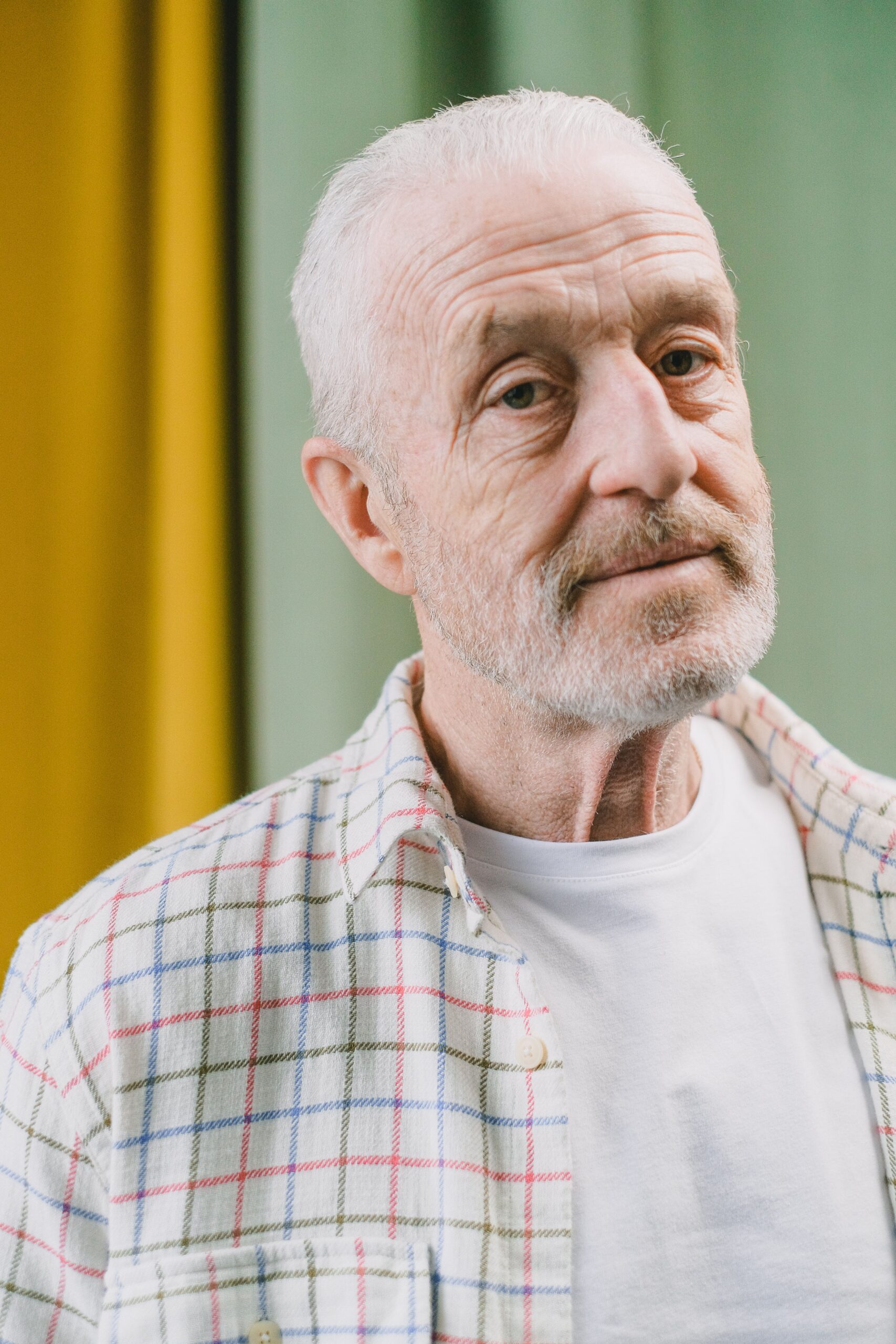 Portrait of an elderly man with a beard in a checkered shirt against a colorful backdrop.